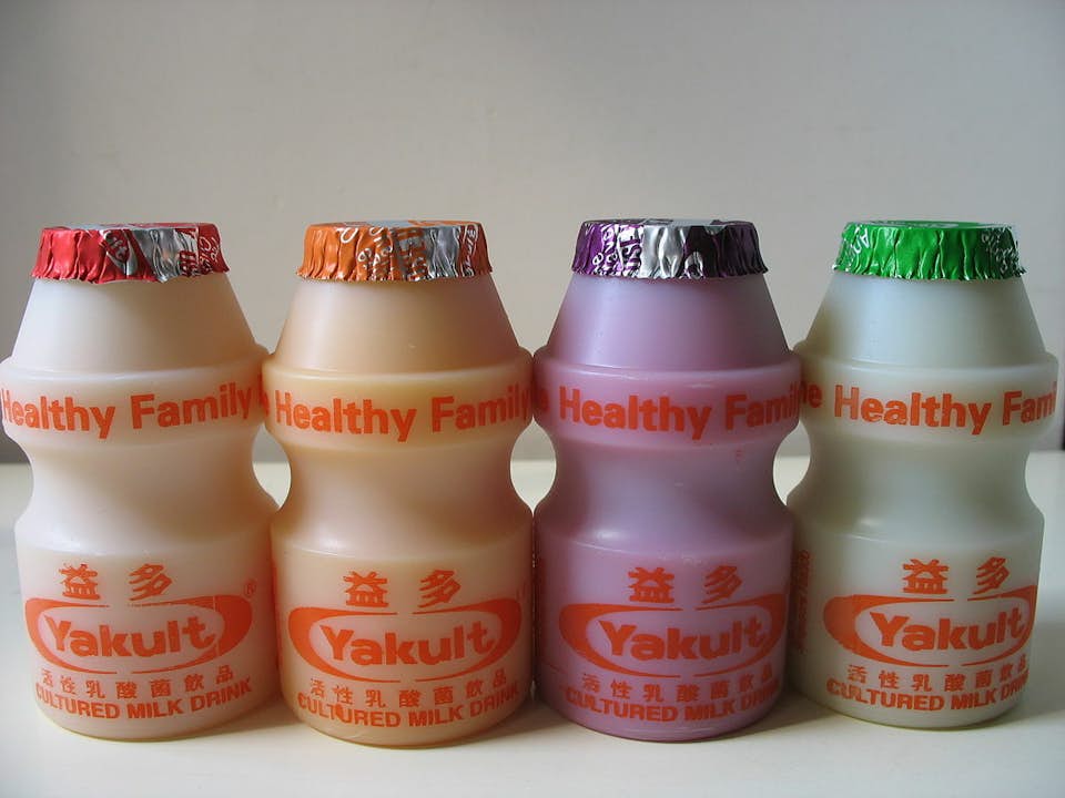 Four yakult bottles of different colors on a flat surface.