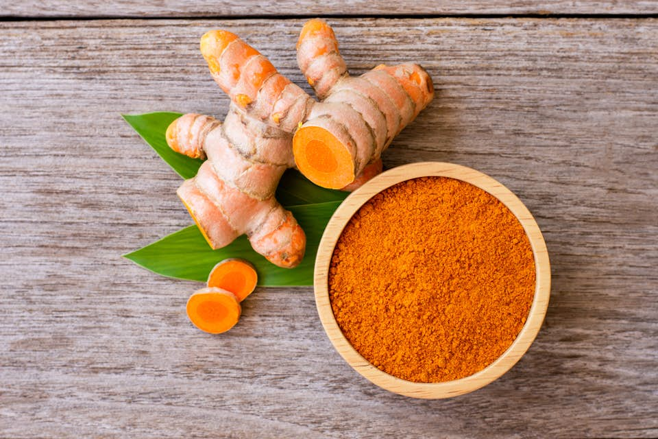 Raw turmeric and powdered turmeric photographed from above on a wooden surface.